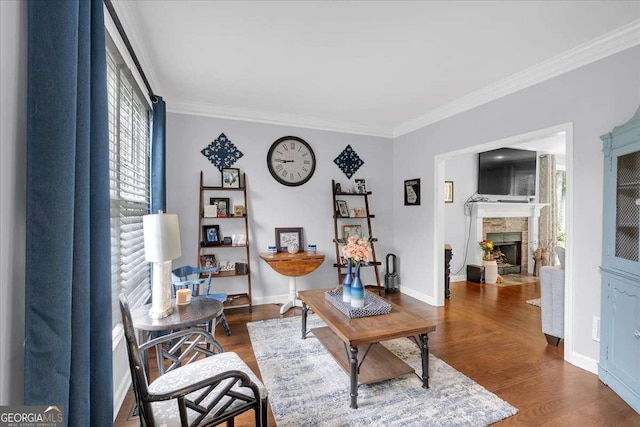 living room with ornamental molding, a tiled fireplace, wood finished floors, and baseboards