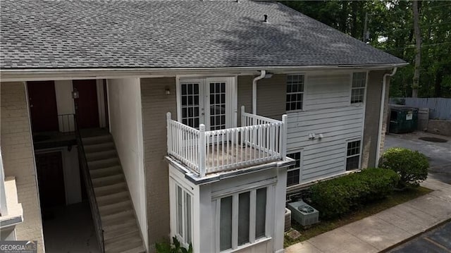 rear view of house featuring roof with shingles, a balcony, and french doors