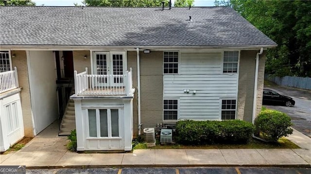 back of property with french doors, cooling unit, brick siding, and roof with shingles