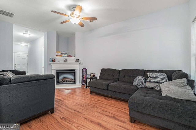 living area with light wood-type flooring, a ceiling fan, and a fireplace with raised hearth