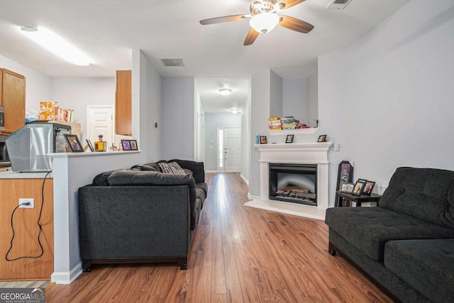 living room with wood finished floors, a ceiling fan, a fireplace with raised hearth, and baseboards