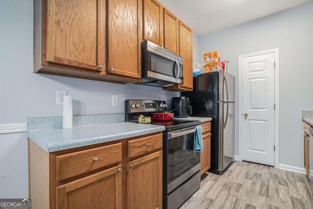 kitchen with appliances with stainless steel finishes, light wood finished floors, brown cabinetry, and light countertops