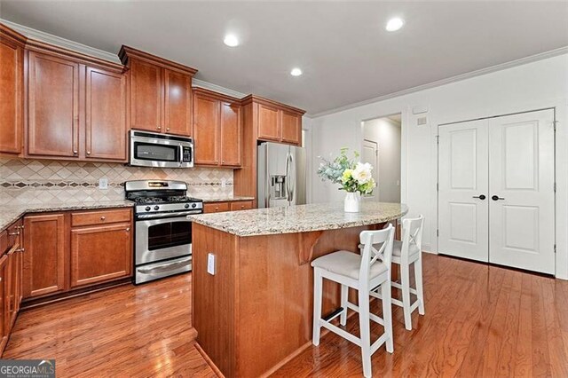 1399 Kilchis Falls Way, Braselton, GA 30517 - kitchen with stainless steel appliances, a center island, light stone countertops, a kitchen bar, and light wood-type flooring