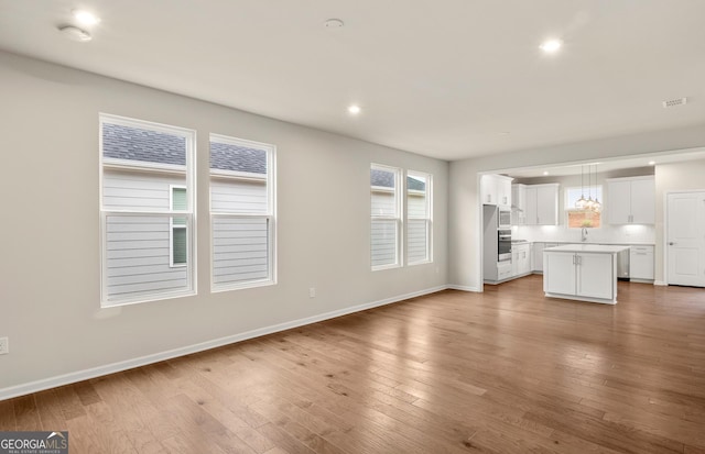 unfurnished living room featuring recessed lighting, baseboards, a sink, and wood finished floors