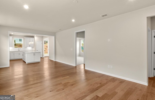unfurnished living room with a sink, light wood finished floors, baseboards, and recessed lighting