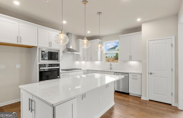 kitchen with stainless steel appliances, wall chimney range hood, a sink, a center island, and white cabinetry
