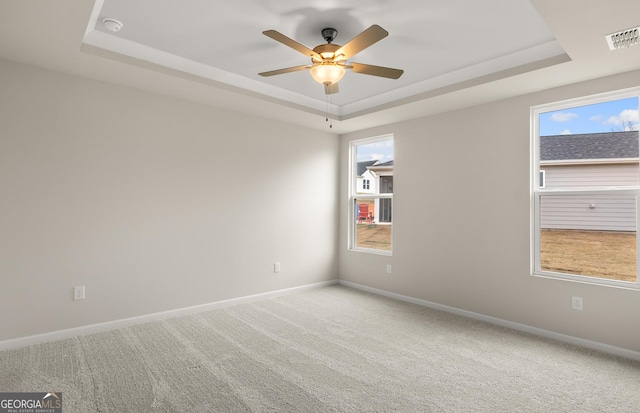 empty room featuring a tray ceiling, ceiling fan, carpet, and baseboards