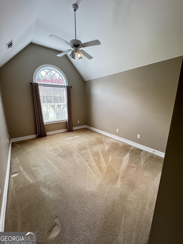 carpeted empty room with a ceiling fan, vaulted ceiling, and baseboards