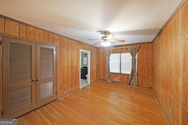 spare room with light wood finished floors, ceiling fan, and wood walls