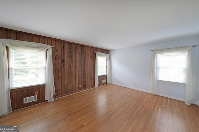 empty room with light wood-style floors, baseboards, and wooden walls