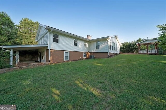 back of property featuring a gazebo, a yard, a chimney, a carport, and central AC
