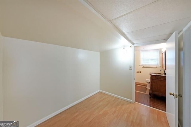 additional living space with light wood-style floors, baseboards, and a sink