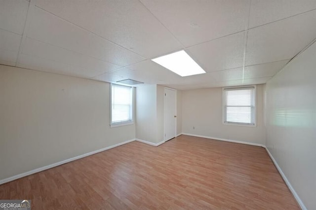 below grade area featuring light wood finished floors, baseboards, healthy amount of natural light, and a paneled ceiling