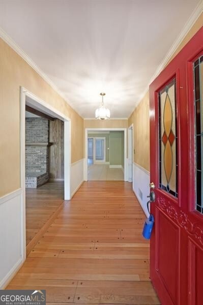 corridor with a chandelier, wainscoting, wood finished floors, and ornamental molding