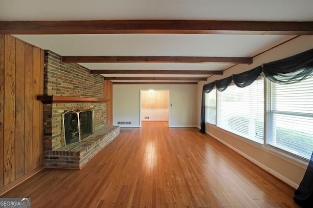 unfurnished living room with baseboards, wood finished floors, beamed ceiling, and a fireplace