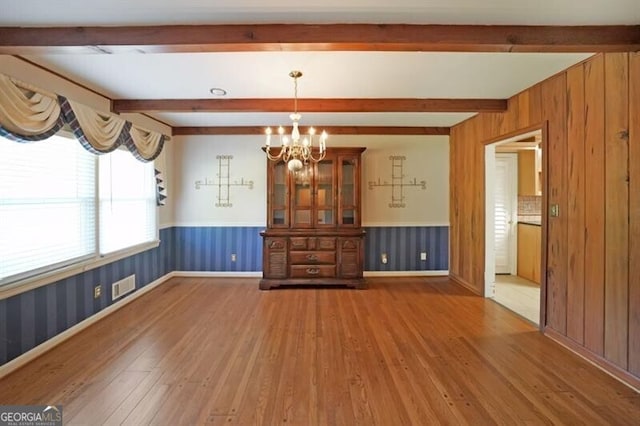unfurnished dining area with hardwood / wood-style flooring, beam ceiling, a chandelier, wainscoting, and baseboards