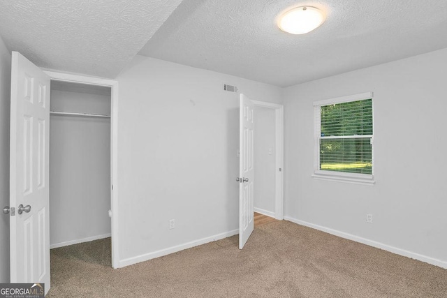 unfurnished bedroom with a textured ceiling, carpet floors, a closet, and baseboards