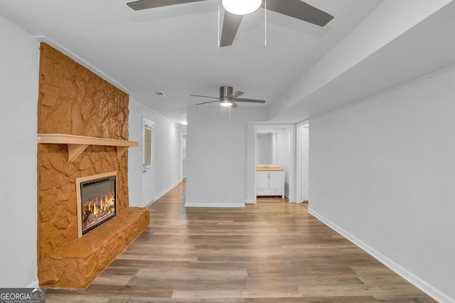 unfurnished living room featuring a ceiling fan, a stone fireplace, wood finished floors, and baseboards