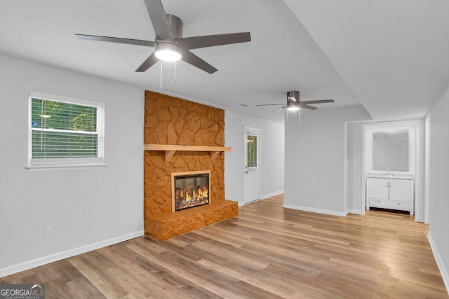 unfurnished living room featuring ceiling fan, baseboards, a fireplace, and wood finished floors