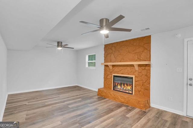 unfurnished living room with ceiling fan, wood finished floors, a stone fireplace, and baseboards