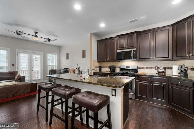 kitchen featuring appliances with stainless steel finishes, a sink, open floor plan, a kitchen breakfast bar, and dark brown cabinetry