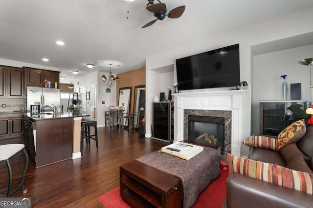 living area with ceiling fan, dark wood-style flooring, a chandelier, a fireplace, and recessed lighting