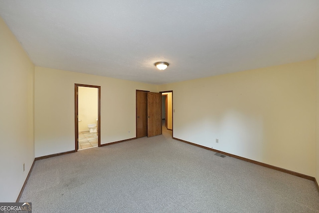 unfurnished bedroom with light colored carpet, baseboards, and connected bathroom
