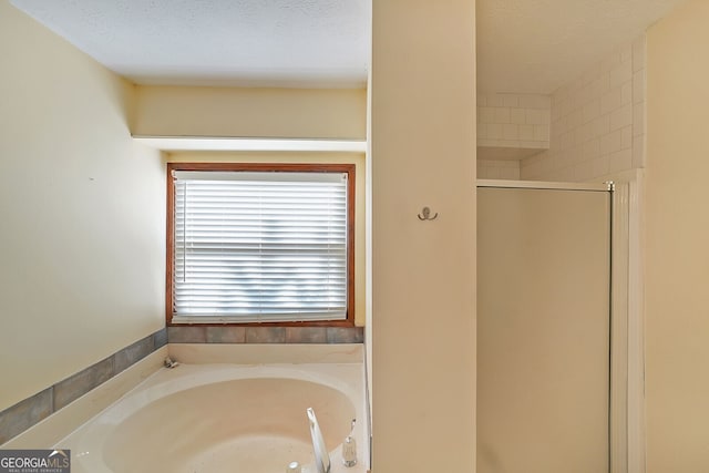 bathroom with a textured ceiling, a bath, and a shower stall