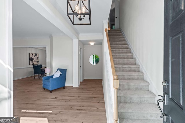 foyer featuring wood finished floors, stairs, crown molding, a chandelier, and baseboards