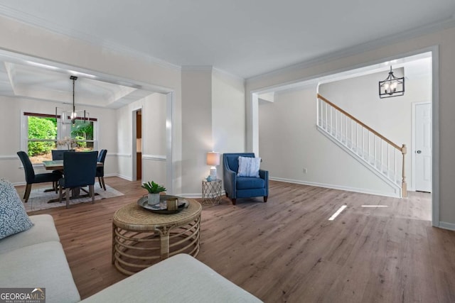 living area with a chandelier, wood finished floors, stairway, baseboards, and crown molding