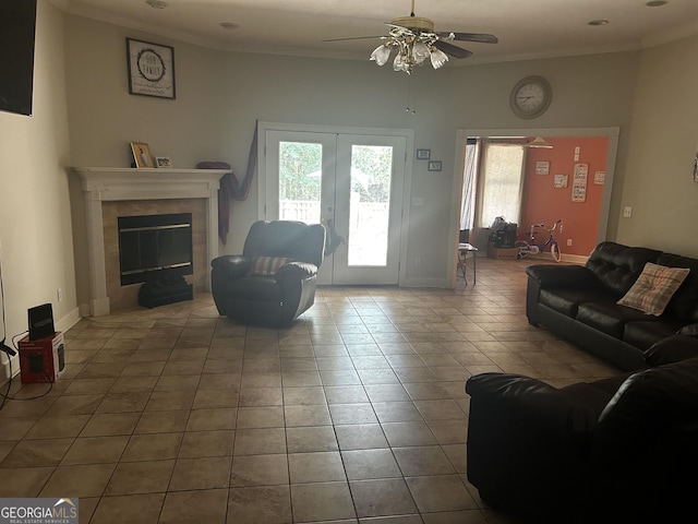 tiled living room featuring ceiling fan, ornamental molding, a tiled fireplace, french doors, and baseboards