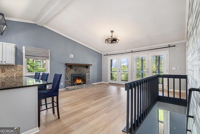 living room with plenty of natural light, french doors, light wood finished floors, a stone fireplace, and ornamental molding