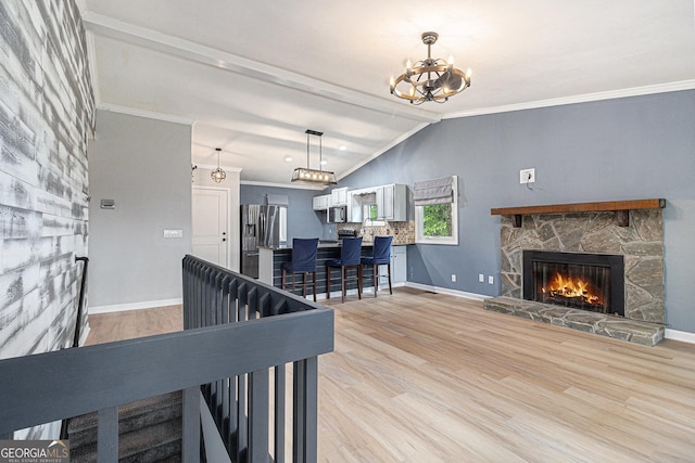 living area featuring a chandelier, a stone fireplace, light wood-style flooring, ornamental molding, and baseboards