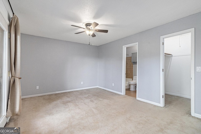 unfurnished bedroom with carpet, a spacious closet, baseboards, and connected bathroom