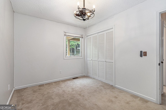 unfurnished bedroom with a chandelier, a closet, carpet, baseboards, and a textured ceiling