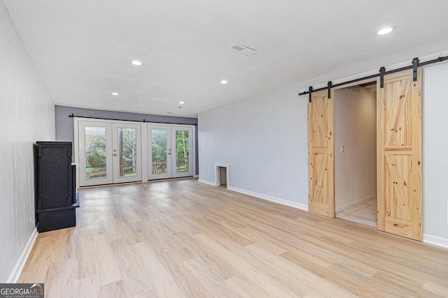 unfurnished living room with a barn door, light wood finished floors, recessed lighting, and baseboards