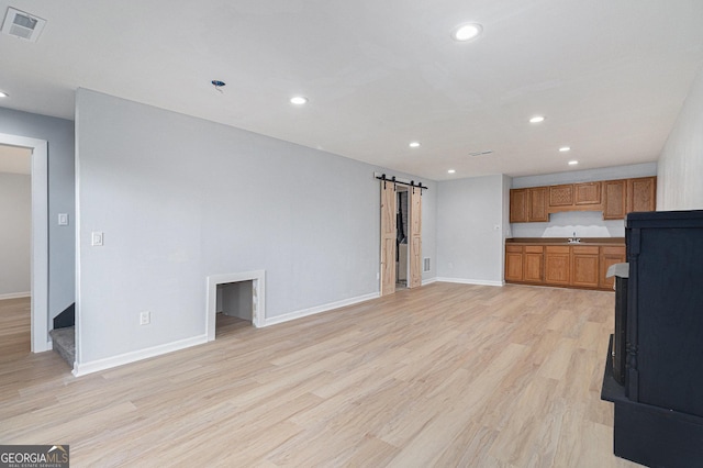 unfurnished living room with a barn door, recessed lighting, baseboards, and light wood-style floors