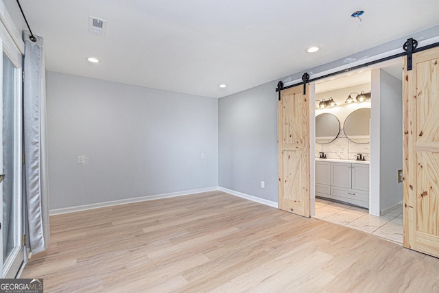 unfurnished bedroom with a barn door, light wood finished floors, recessed lighting, baseboards, and ensuite bath