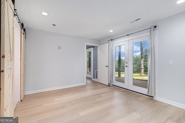 empty room with a barn door, french doors, light wood-style flooring, recessed lighting, and baseboards