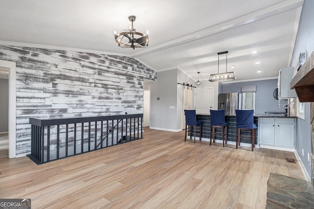kitchen with a chandelier, a barn door, an accent wall, vaulted ceiling, and light wood-style floors