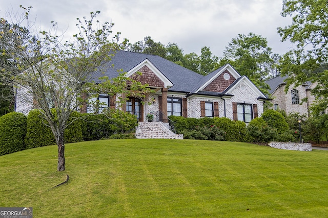 craftsman house featuring a front yard, brick siding, and a shingled roof