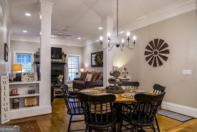 dining space with crown molding, decorative columns, dark wood-type flooring, ceiling fan, and a fireplace