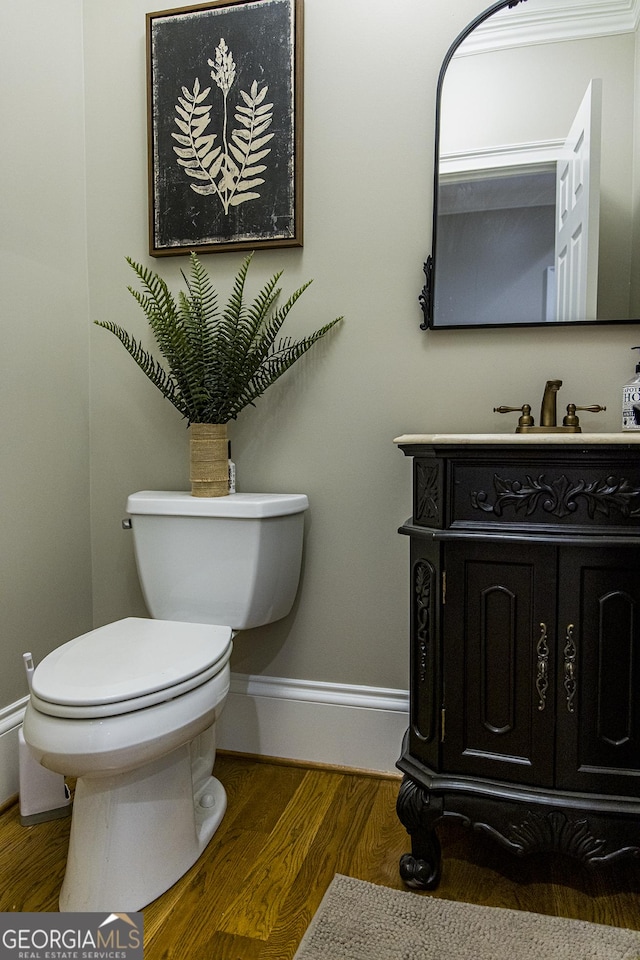 half bath featuring toilet, vanity, baseboards, and wood finished floors