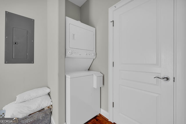 clothes washing area with stacked washer / dryer, electric panel, baseboards, and dark wood finished floors
