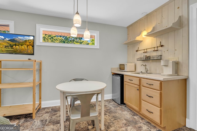 kitchen with white microwave, stone finish floors, a sink, light brown cabinets, and baseboards