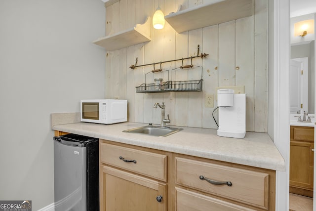 kitchen with stainless steel fridge, a sink, white microwave, light brown cabinetry, and light countertops