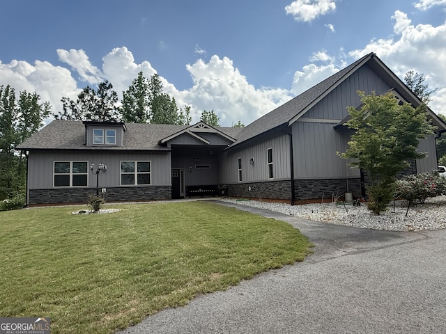 view of front facade with stone siding, roof with shingles, and a front lawn