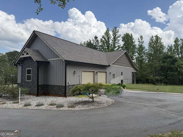 view of home's exterior featuring a garage, board and batten siding, stone siding, asphalt driveway, and roof with shingles