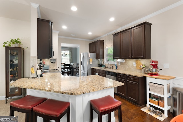 kitchen featuring appliances with stainless steel finishes, dark brown cabinetry, ornamental molding, a peninsula, and a kitchen bar