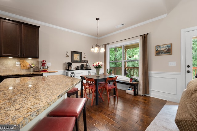 dining room featuring a chandelier, dark wood finished floors, ornamental molding, and wainscoting
